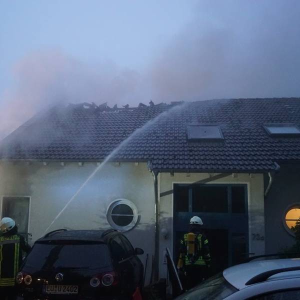 Feuerwehrleute bekämpfen den Brand des Hauses, dessen Dach bereits zum Teil zerstört worden ist.