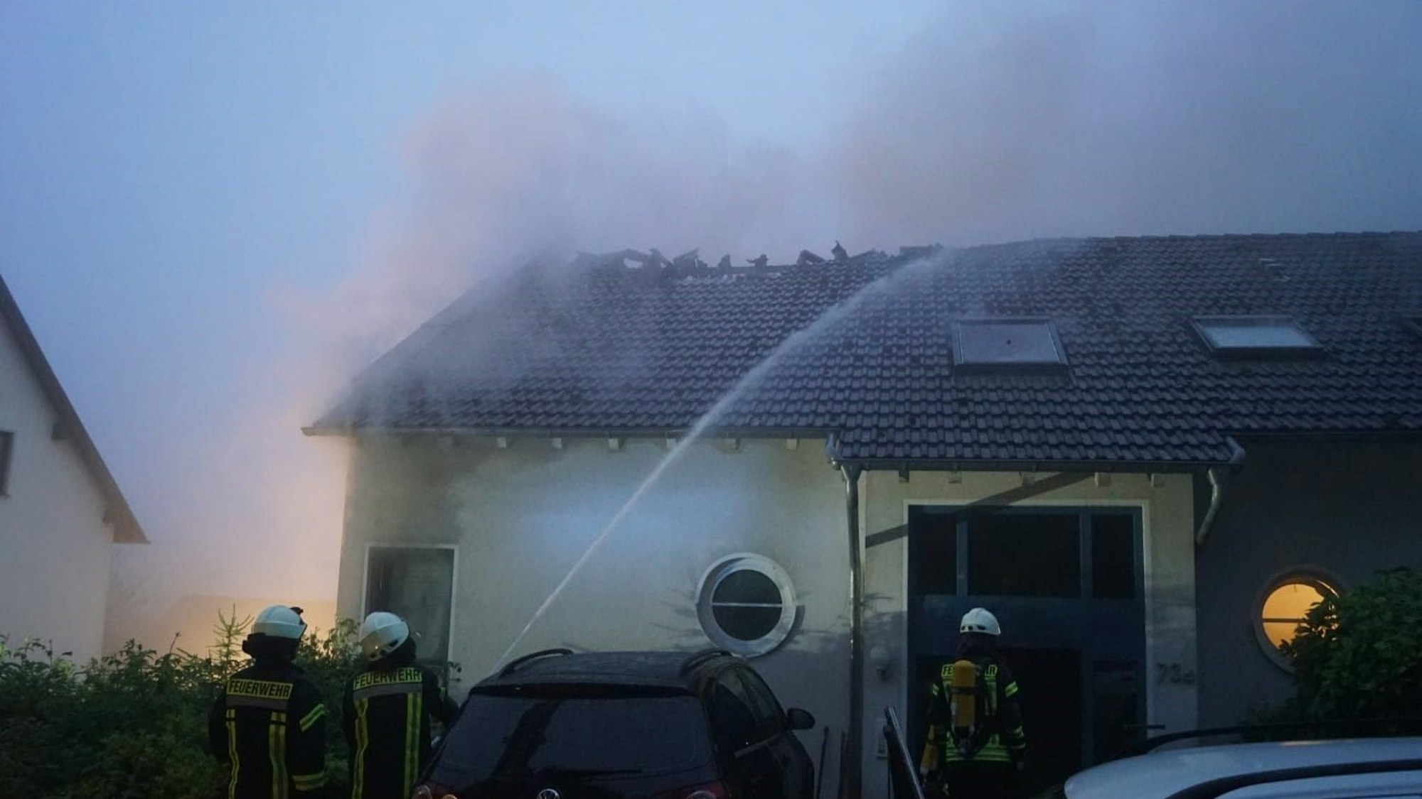 Feuerwehrleute bekämpfen den Brand des Hauses, dessen Dach bereits zum Teil zerstört worden ist.