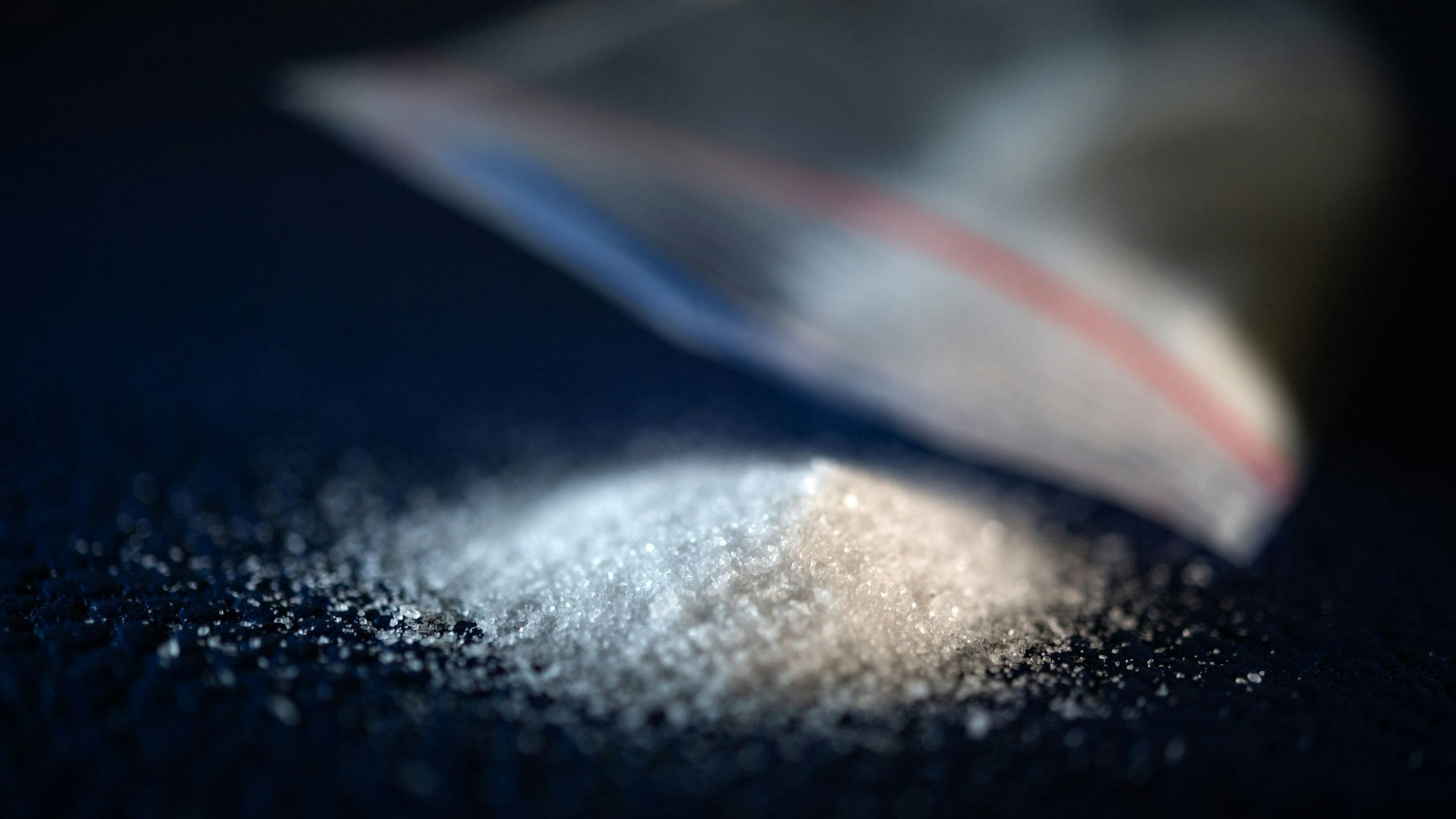 Ein Feststoff liegt auf einer blauen Unterlage neben einem Kunststoff-Tütchen (gestellte Szene)