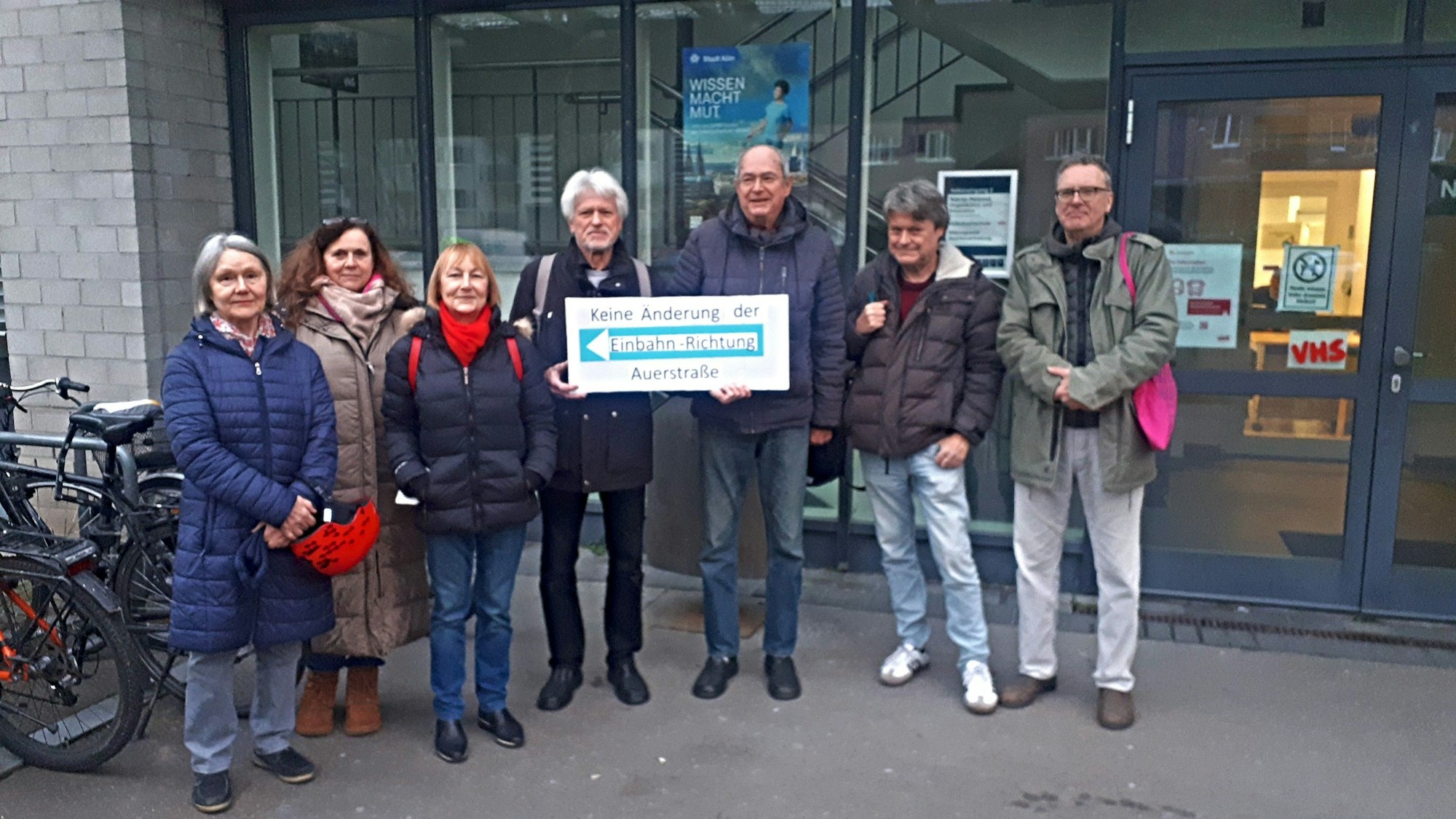 Drei Frauen und vier Männer stehen vor dem Gebäude der Bezirksvertretung Nippes und halten ein Schild auf dem steht Keine Änderung der Einbahn-Richtung Auerstraße.