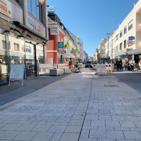 Das Foto zeigt die Fußgängerzone mit frisch verlegtem Pflaster, im Hintergrund Bauzäune, Arbeiter und Passanten.