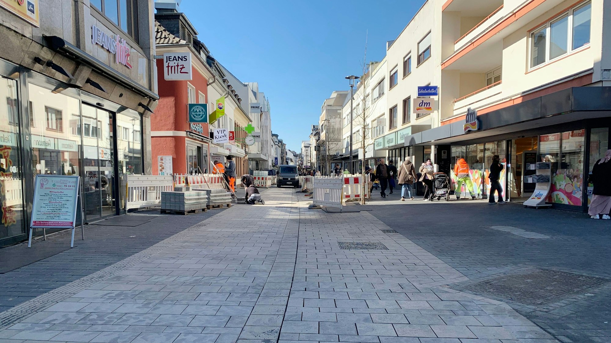 Das Foto zeigt die Fußgängerzone mit frisch verlegtem Pflaster, im Hintergrund Bauzäune, Arbeiter und Passanten.