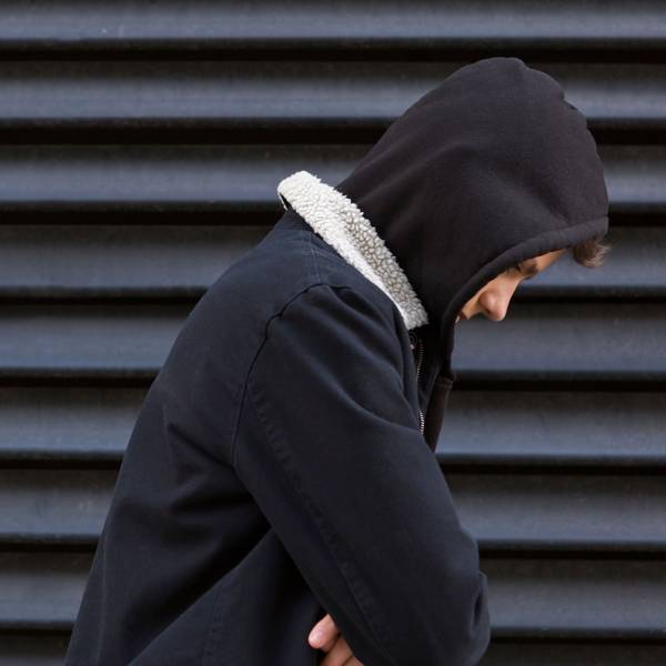 Ein Jugendlicher vor einer schwarzen Wand in schwarzem Pullover schaut traurig nach unten.