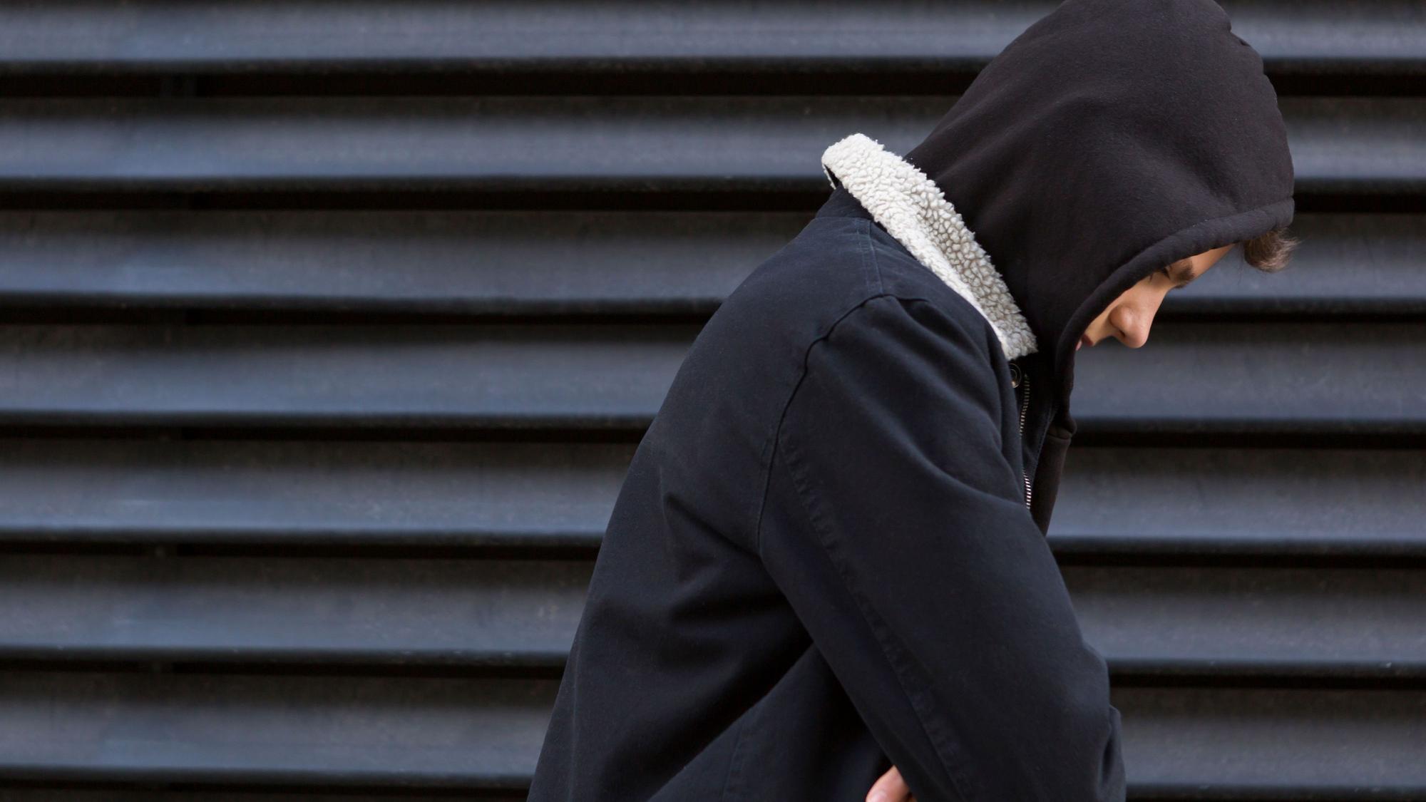 Ein Jugendlicher vor einer schwarzen Wand in schwarzem Pullover schaut traurig nach unten.