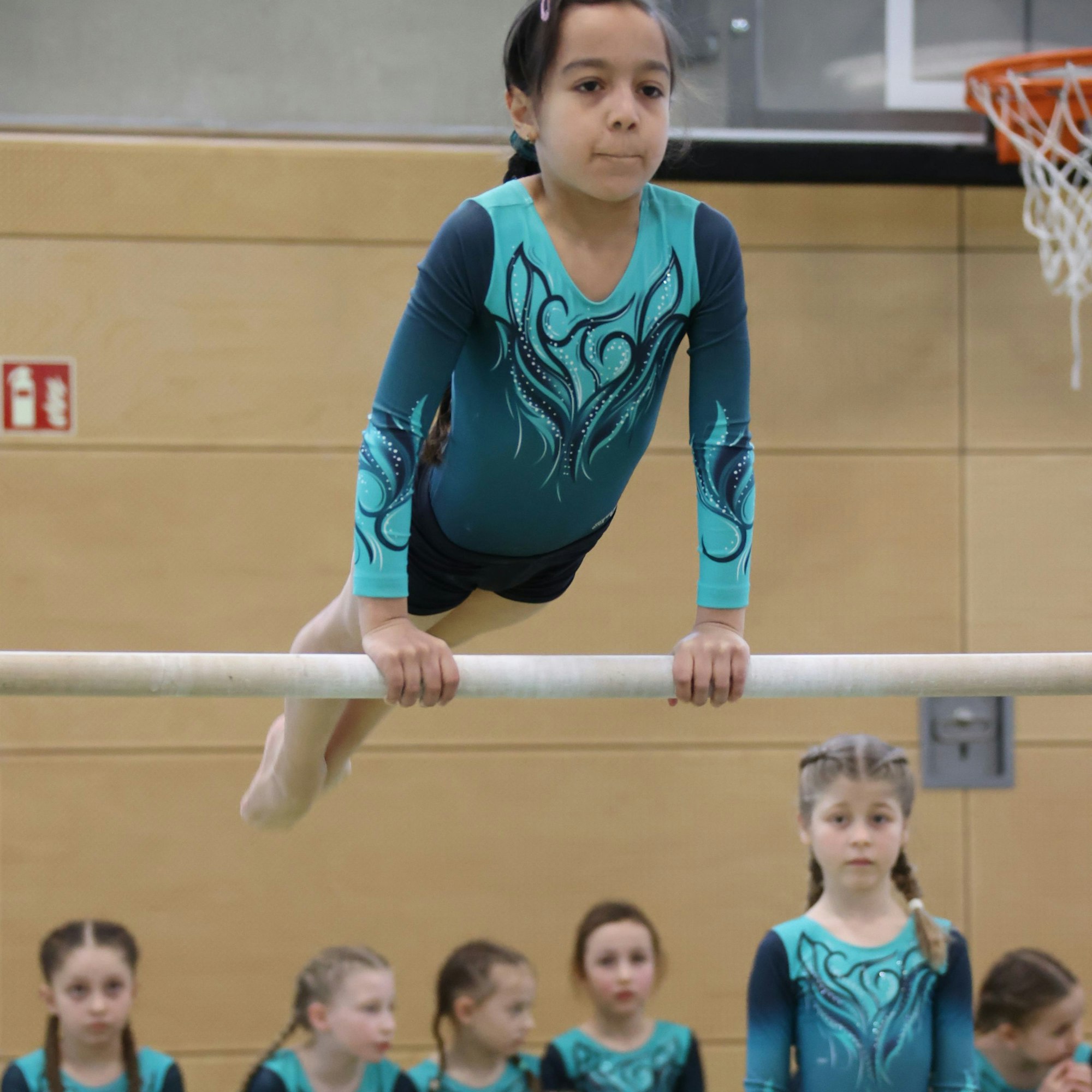 Eine Euskirchener Turnerin stemmt sich auf de Reckstange. Im Hintergrund schauen weitere Turnerinnen zu.