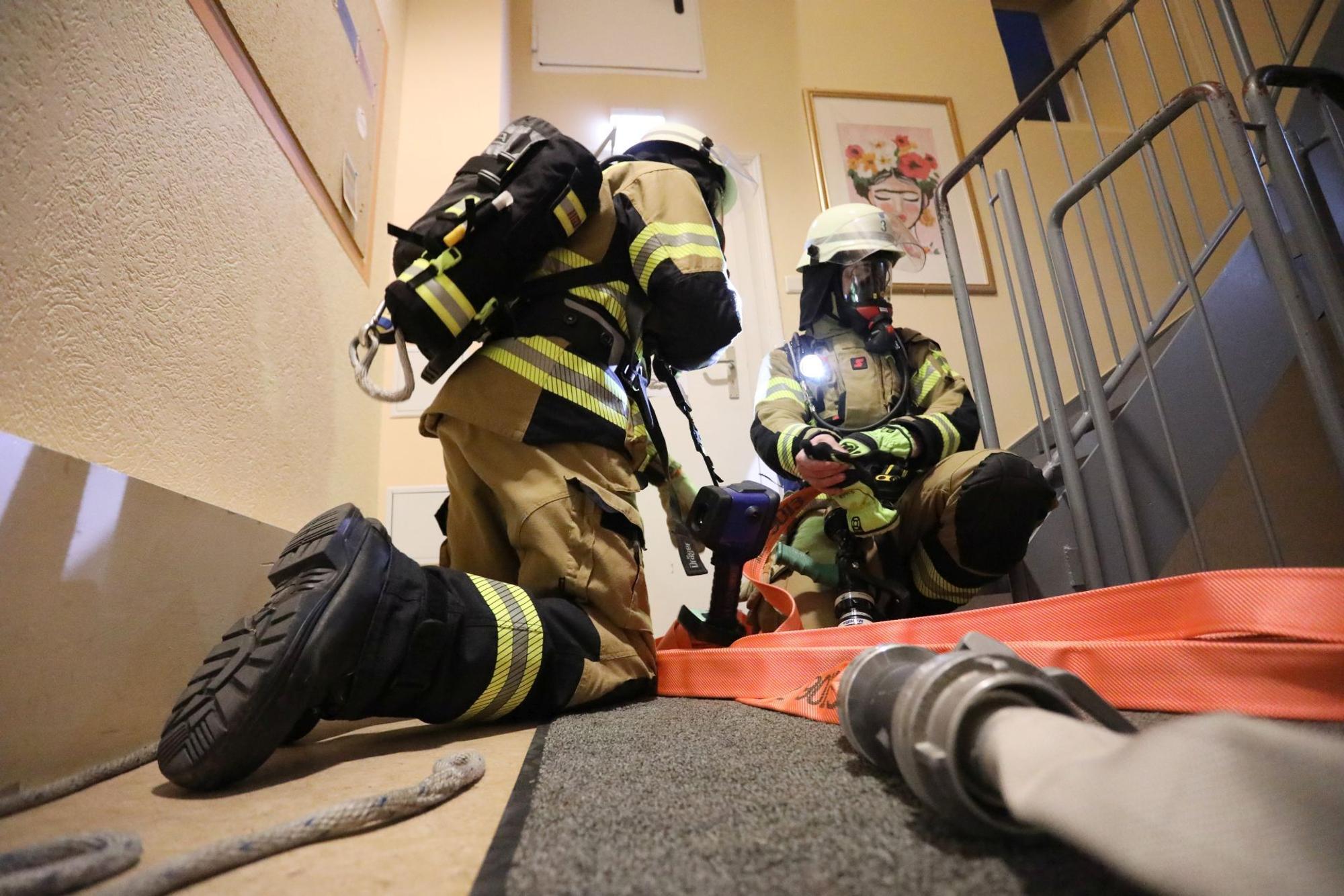 Zwei Feuerwehrleute mit Schläuchen und unter Atemschutz im Flur eines Gebäudes.