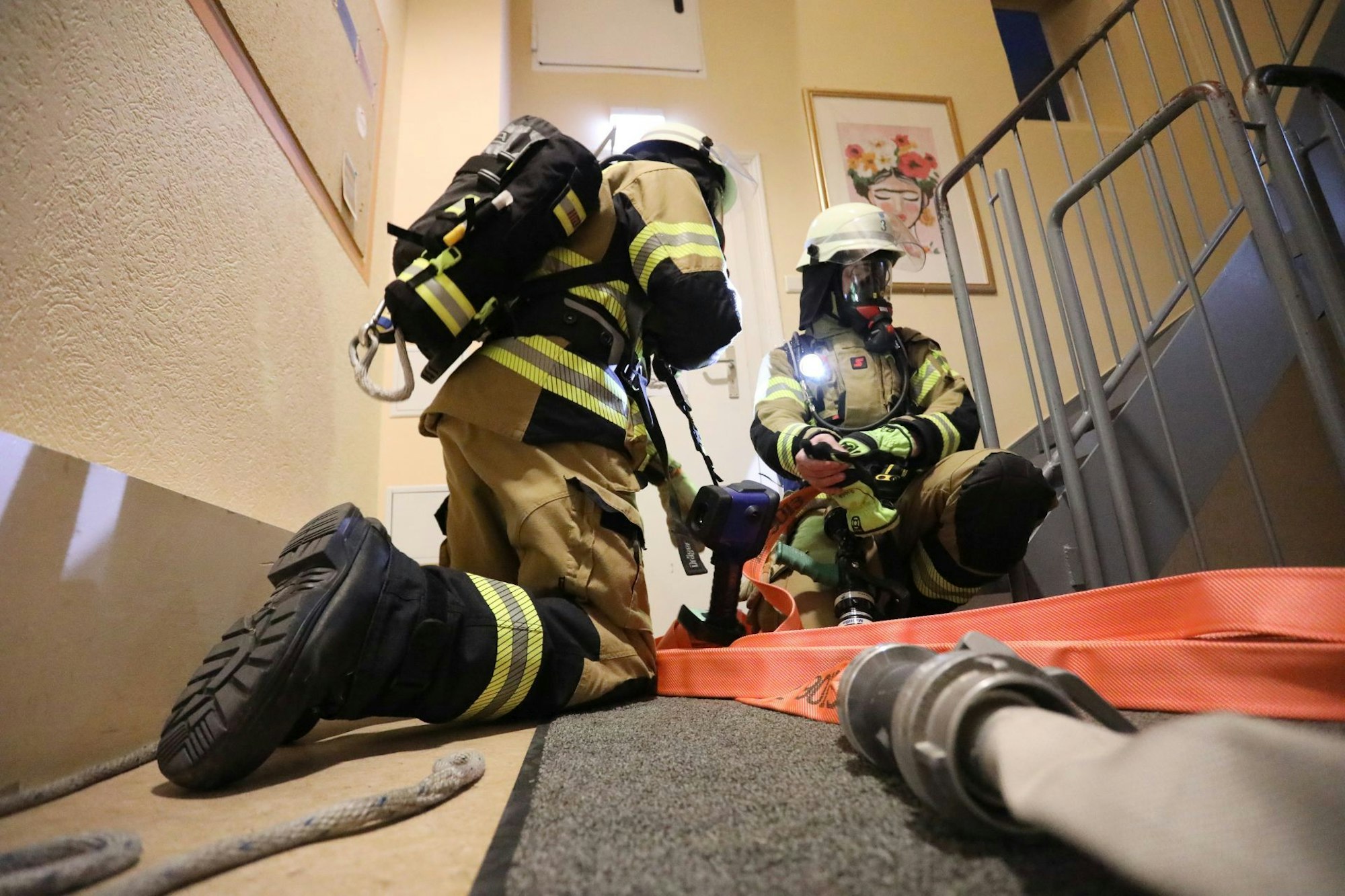 Zwei Feuerwehrleute mit Schläuchen und unter Atemschutz im Flur eines Gebäudes.