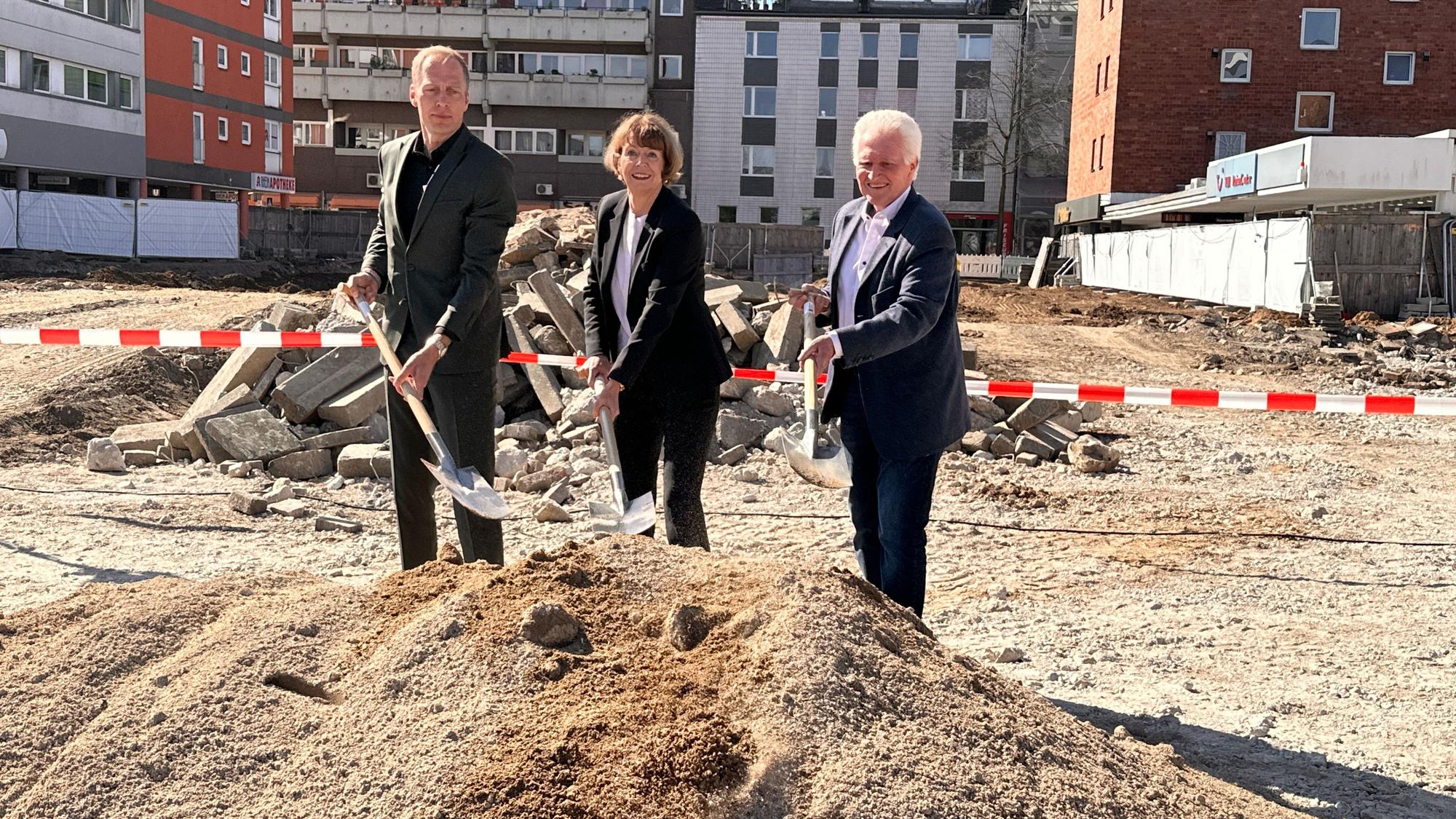 Drei Personen führen einen Spatenstich an einer Baustelle durch.