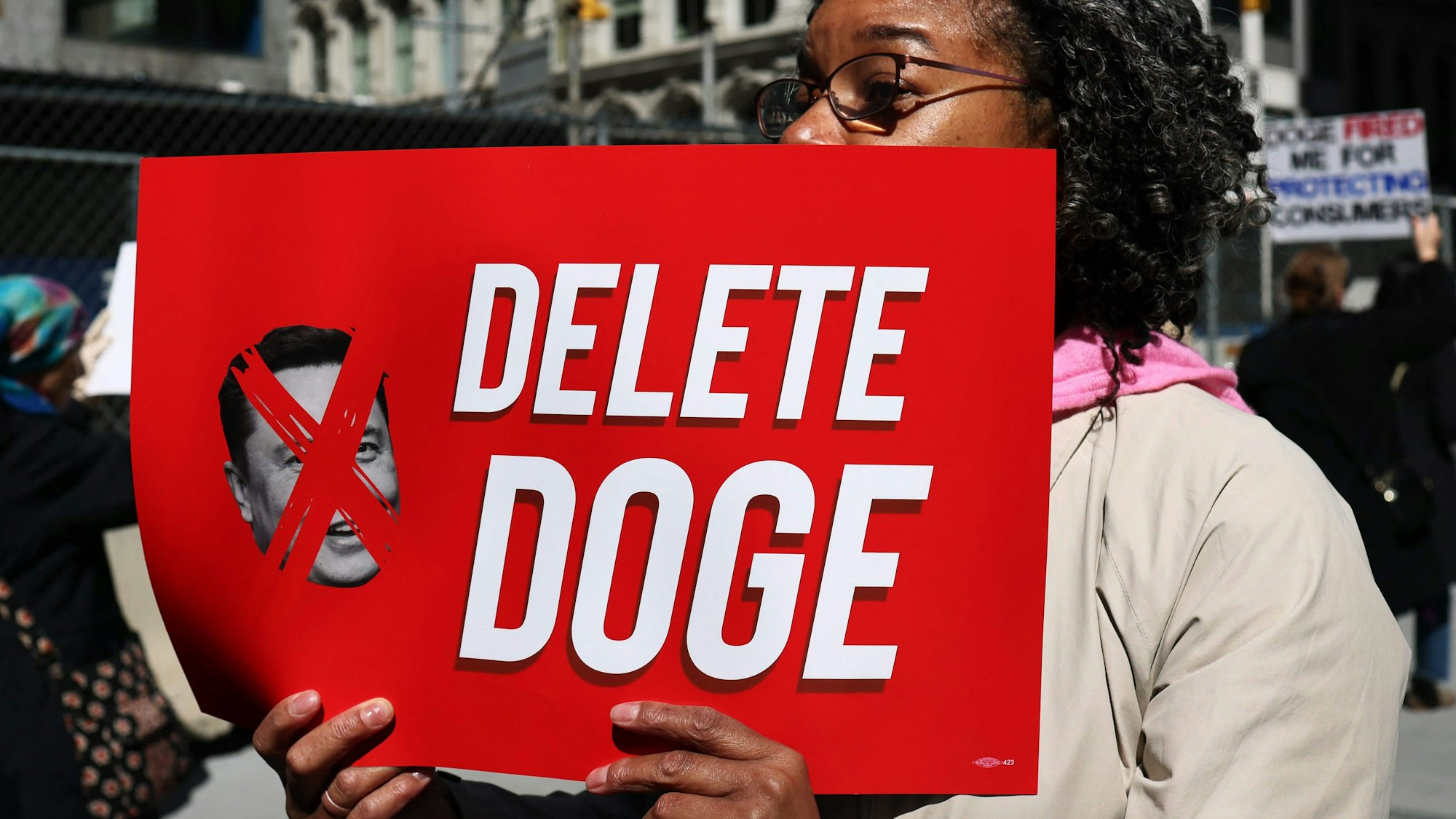 Eine Frau hält bei Protesten in New York ein Schild mit der Aufschrift „Delete Doge“ („Löscht Doge“). Elon Musks Regierungsgremium trägt den Namen „Doge“ und fährt einen radikalen Sparkurs bei US-Behörden. (Archivbild)