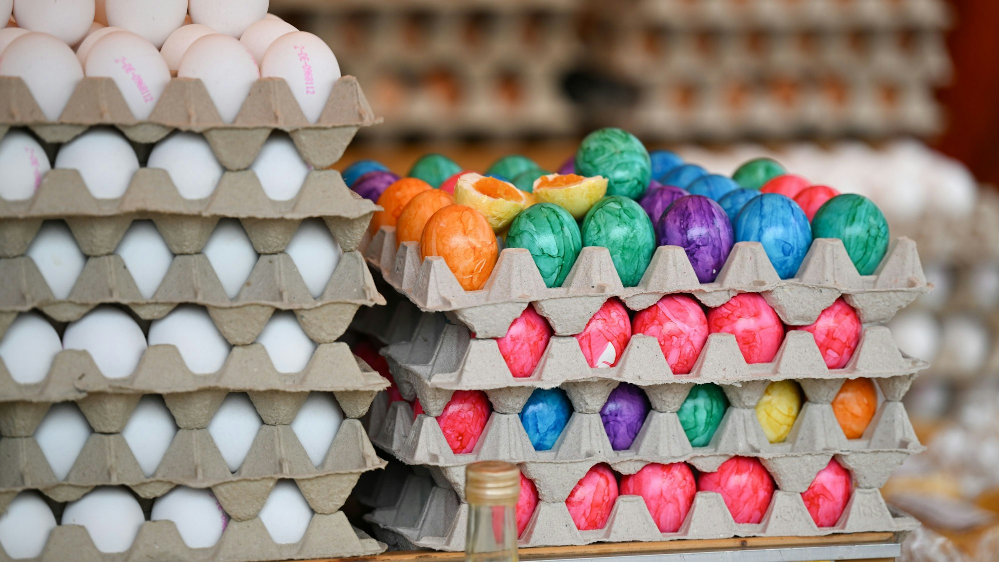 Frische weiße Eier aus Bodenhaltung (l) sowie bunt gefärbte und hartgekochte Eier liegen in einem Marktstand auf dem Wochenmarkt im Stadtteil Bornheim zum Verkauf bereit.