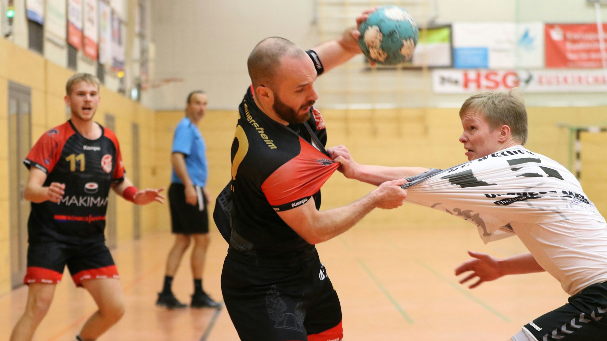 Simon Schöller hält mit der linken Hand den Ball in die Höhe und greift mit der rechten nach dem Trikot seines Gegenspielers, der ihn am Schlafittchen gepackt hat.