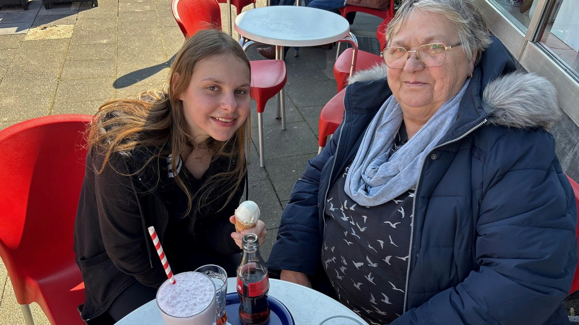 Auf dem Bild ist eine Frau mit ihrer Enkelin zu sehen, die auf der Terrasse eines Eiscafés sitzen.