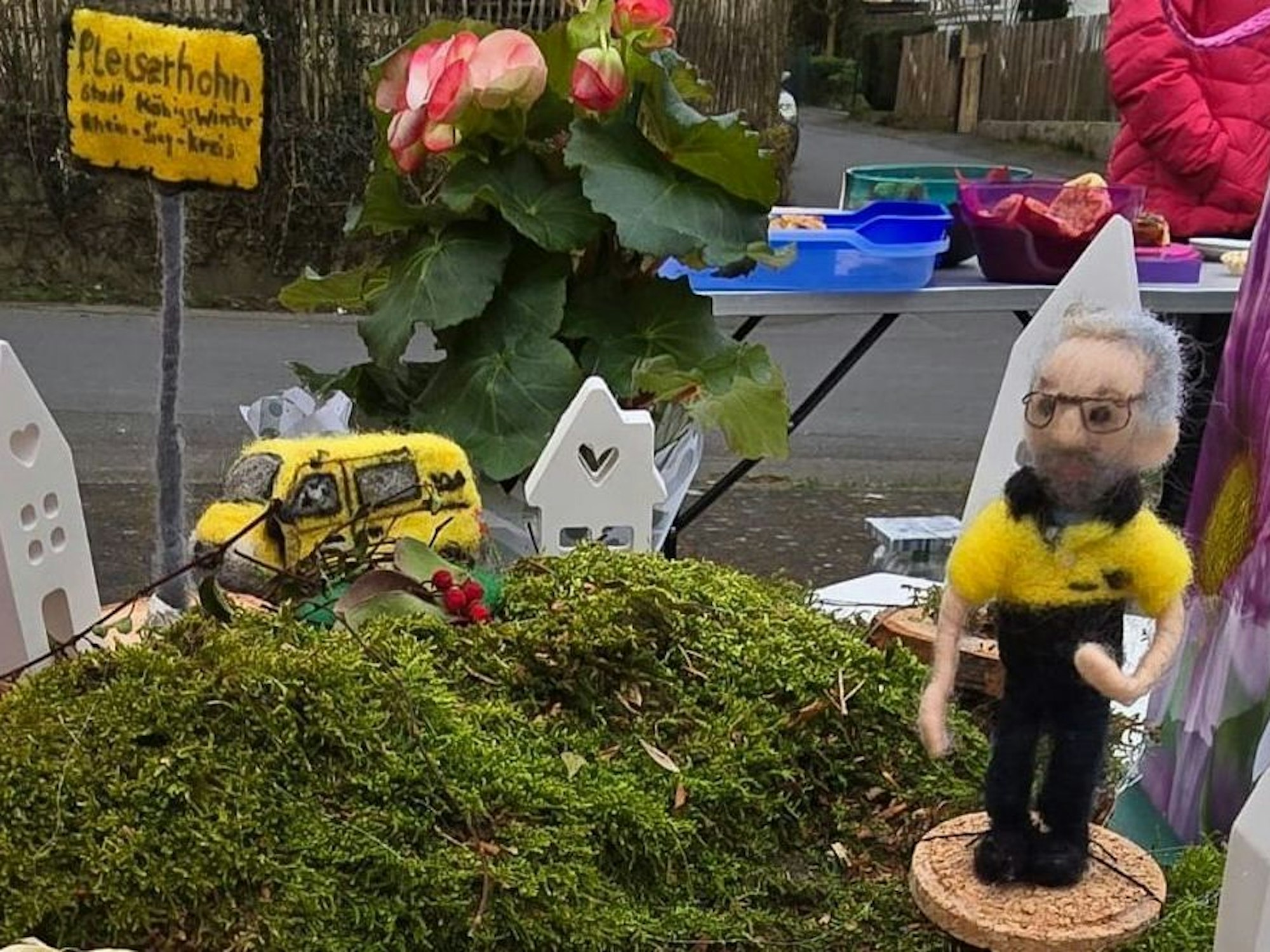 Eine Filzfigur, Auto, Häuser und Straßenschild auf einem Untergrund aus Moos.