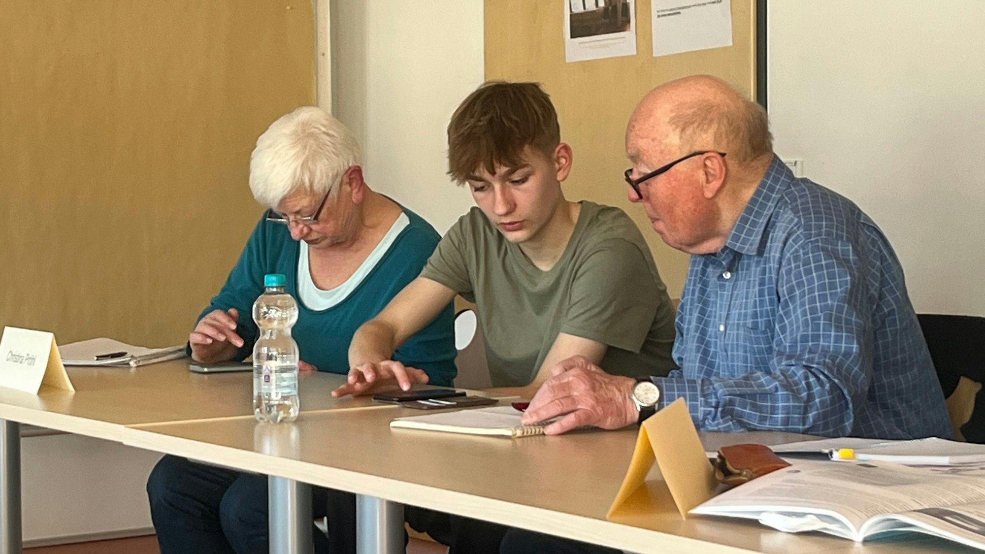 Ein Jugendlicher sitzt am Tisch mit einem älteren Paar zusammen.
