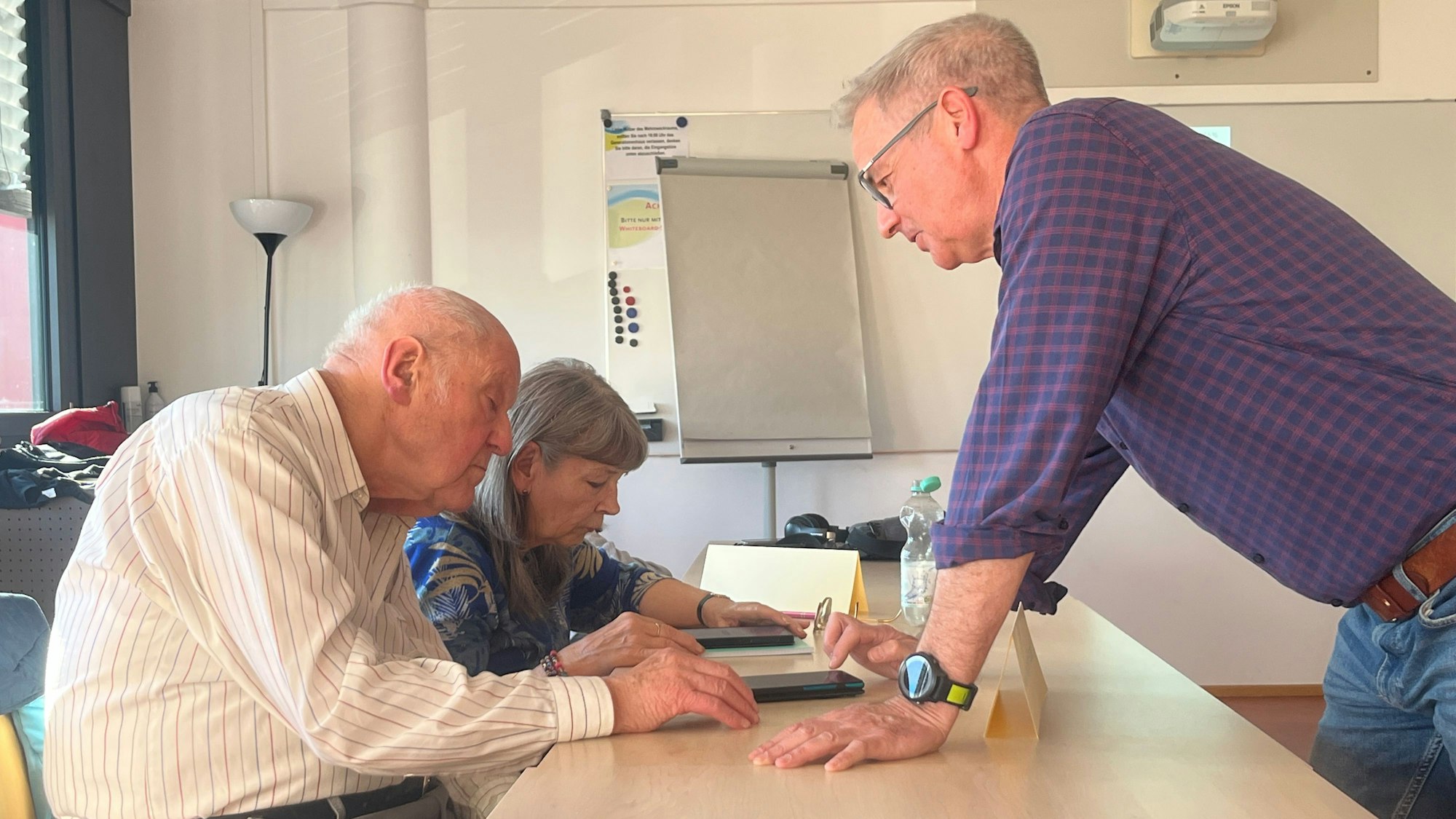 Ein Mann steht vor an einem Tisch vor einem älteren Ehepaar.