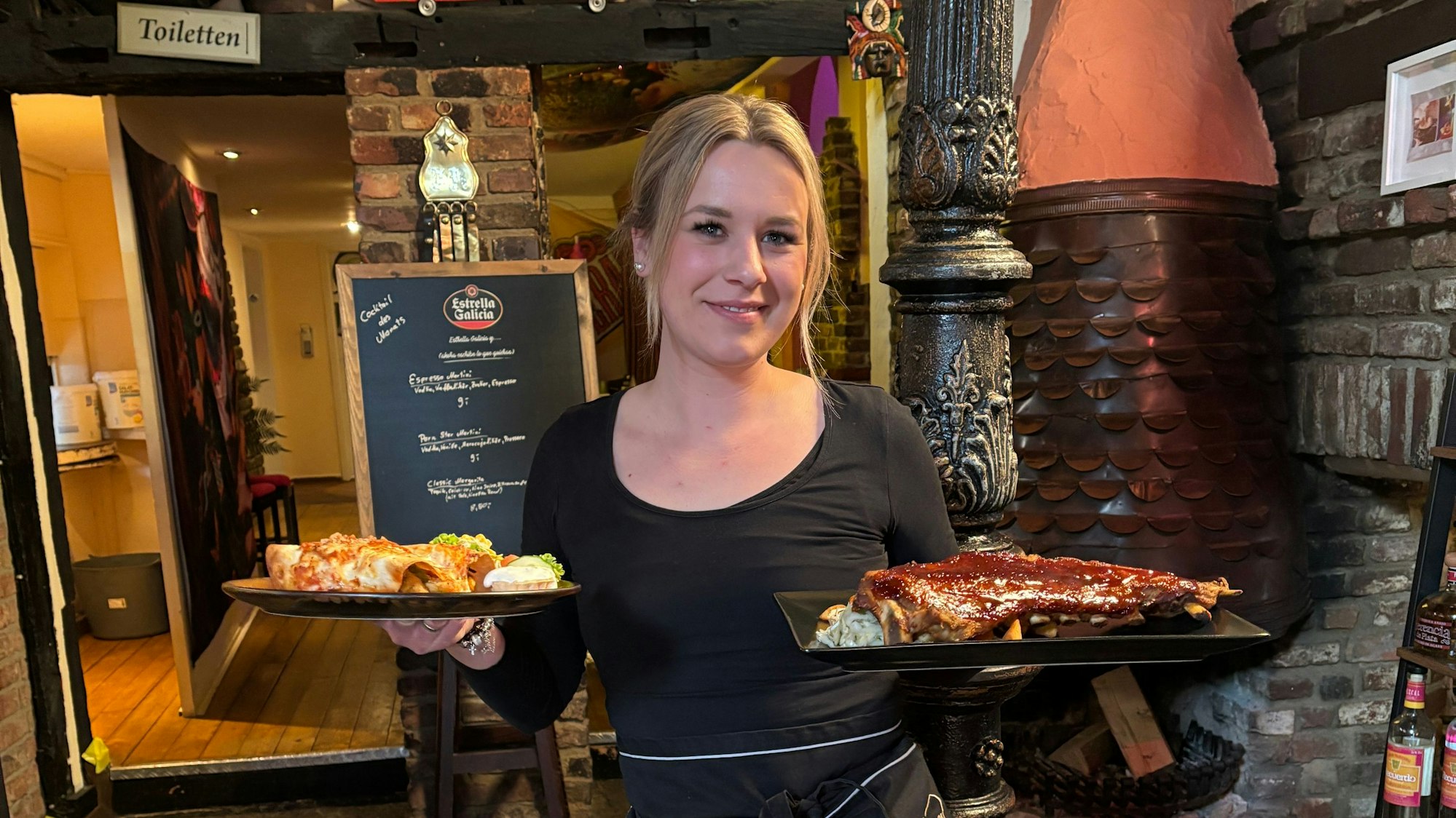Das Foto zeigt eine junge Frau, die zwei Teller in einem Restaurant trägt.