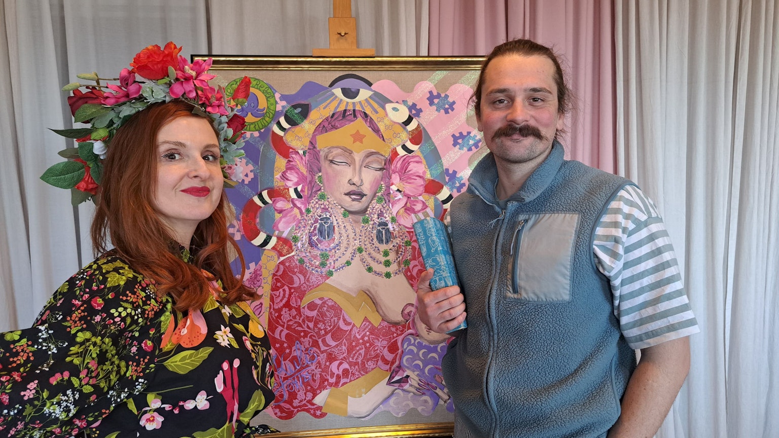 Eine Frau und ein Mann stehen vor einem bunten Gemälde, das eine Göttin zeigt.