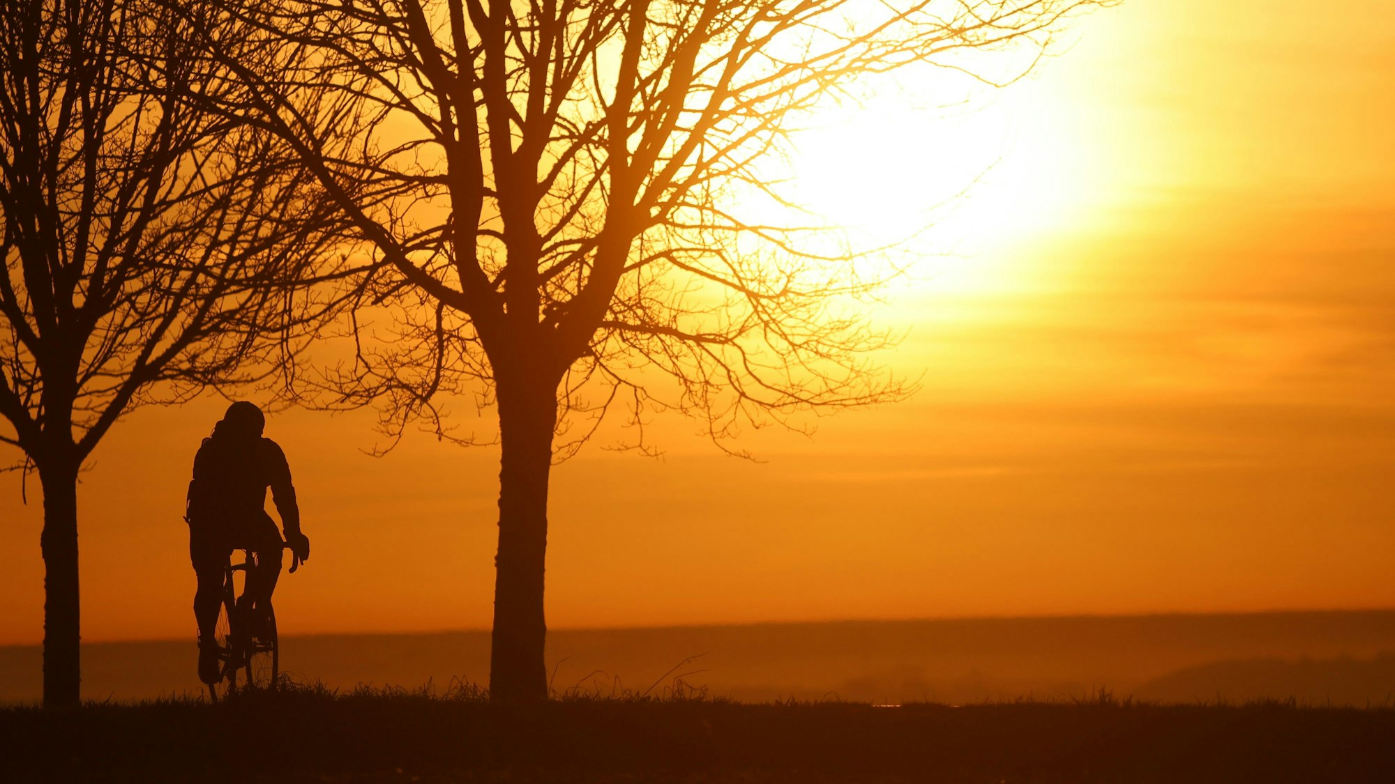 Ein Radfahrer ist am Morgen kurz nach Sonnenaufgang unterwegs, während sich der Himmel durch den Saharastaub in Orangetönen verfärbt hat.