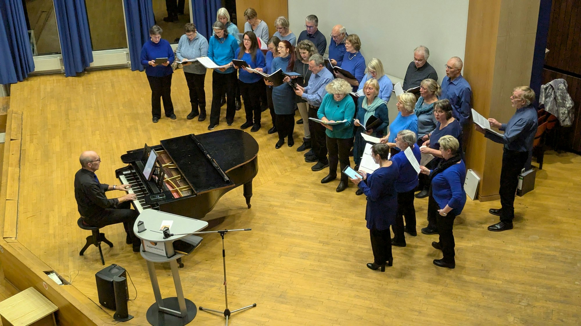 Ein gemischter Chor, der Dirigent sitzt an einem Flügel.