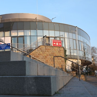 Eine große Treppenanlage und im Hintergrund ein ovales Gebäude mit einer Glasfront.