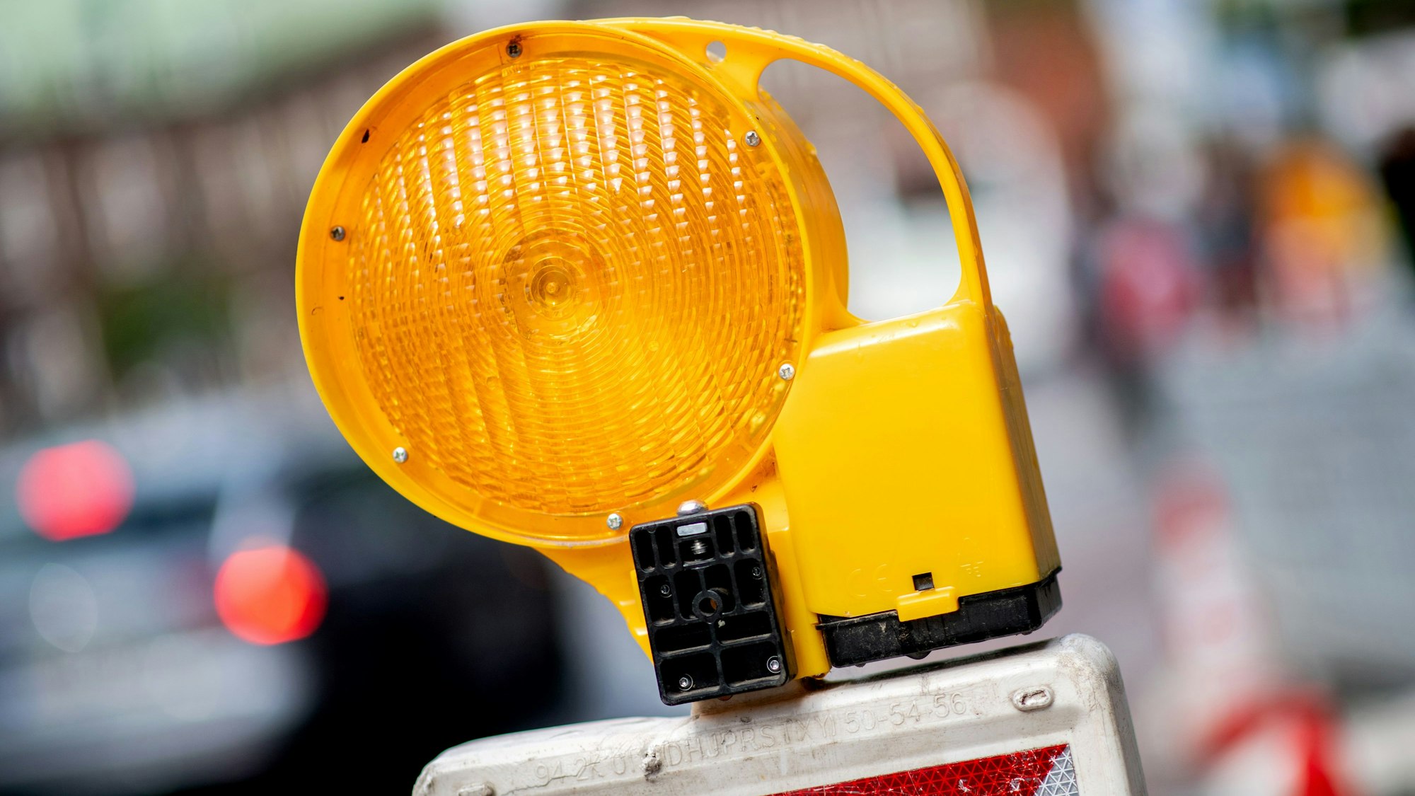 Eine Warnbake mit einer Leuchte darauf steht im Straßenverkehr. Im Hintergrund fahren Autos.