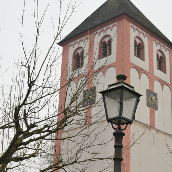 Eine historische Straßenlaterne vor einem romanischen Kirchturm.