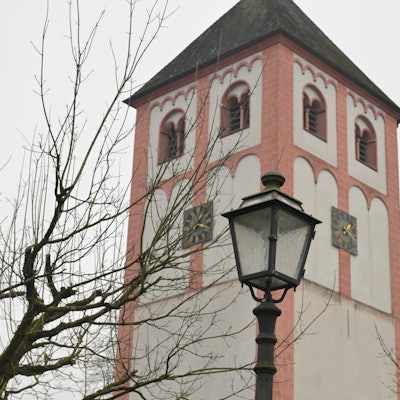 Eine historische Straßenlaterne vor einem romanischen Kirchturm.
