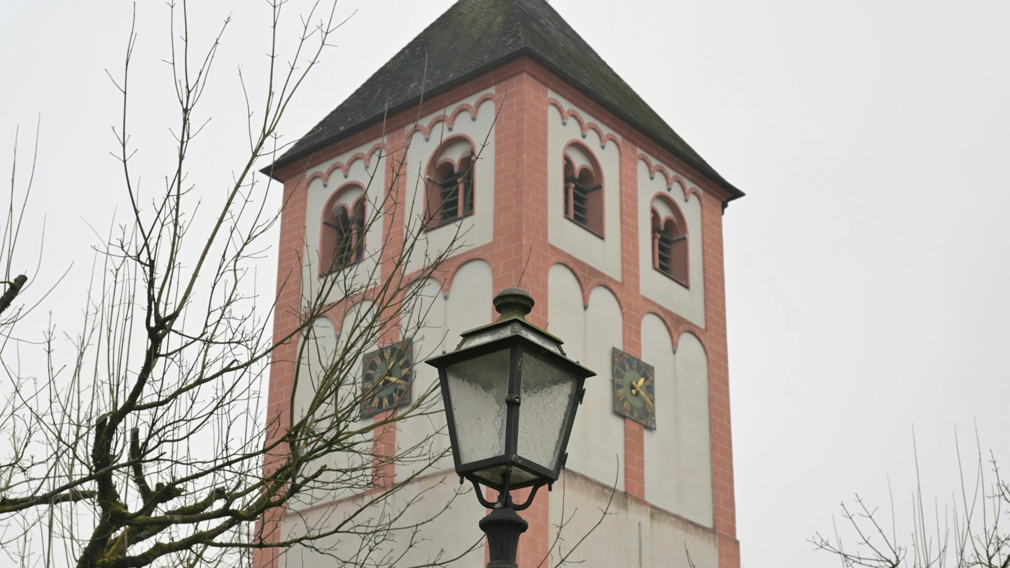 Eine historische Straßenlaterne vor einem romanischen Kirchturm.