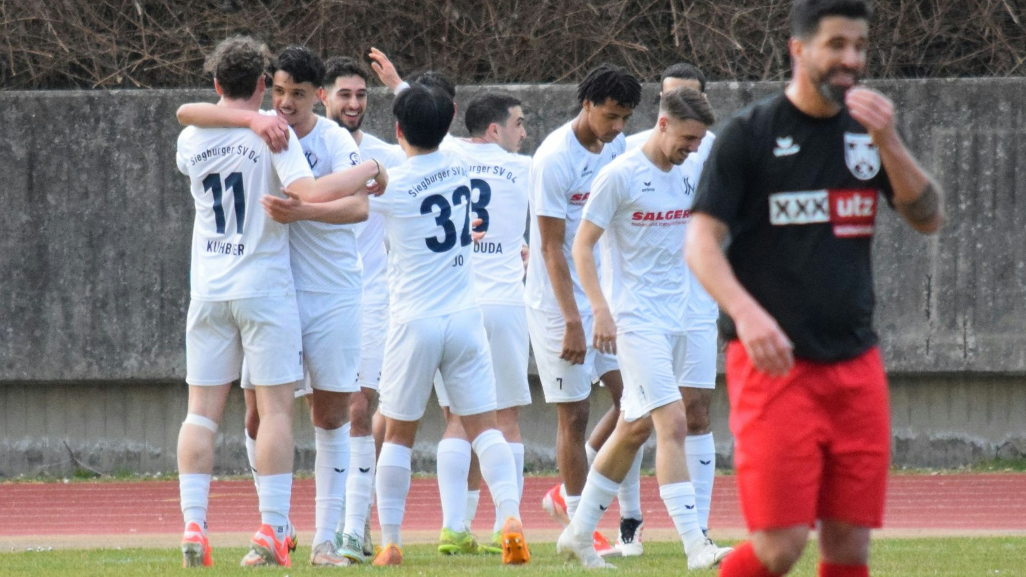 Die Siegburger bejubeln den Führungstreffer, Nils Teixeira vom FC Hennef 05 lächelt nur nach außen hin.