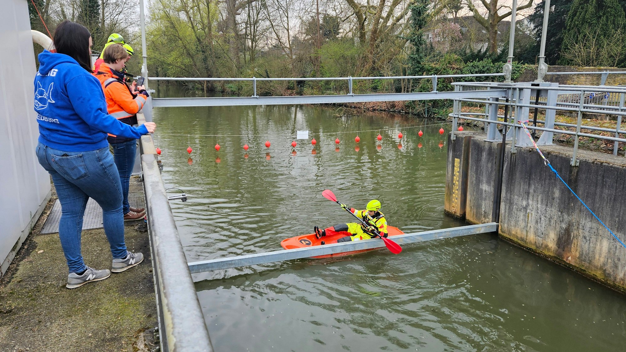 Zu sehen ist ein Kajak, das an einem Metallbalken vor einem Wehr hängen bleibt.