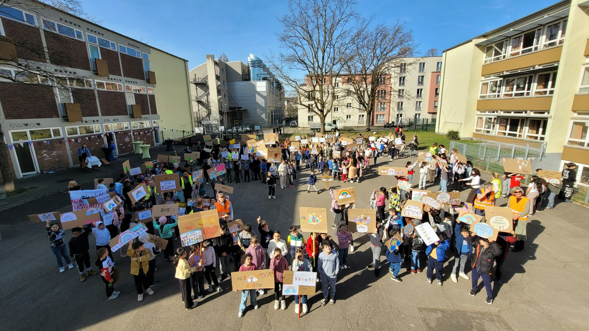 Zahlreiche Schulkinder stehen auf einem Schulhof und halten selbsterstellte Plakate in die Höhe.