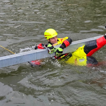 Zu sehen ist ein Strömungsretter der DLRG, der sich an einen Rettungsbalken im Wasser klammert.