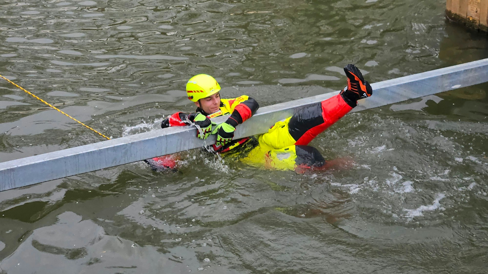 Zu sehen ist ein Strömungsretter der DLRG, der sich an einen Rettungsbalken im Wasser klammert.