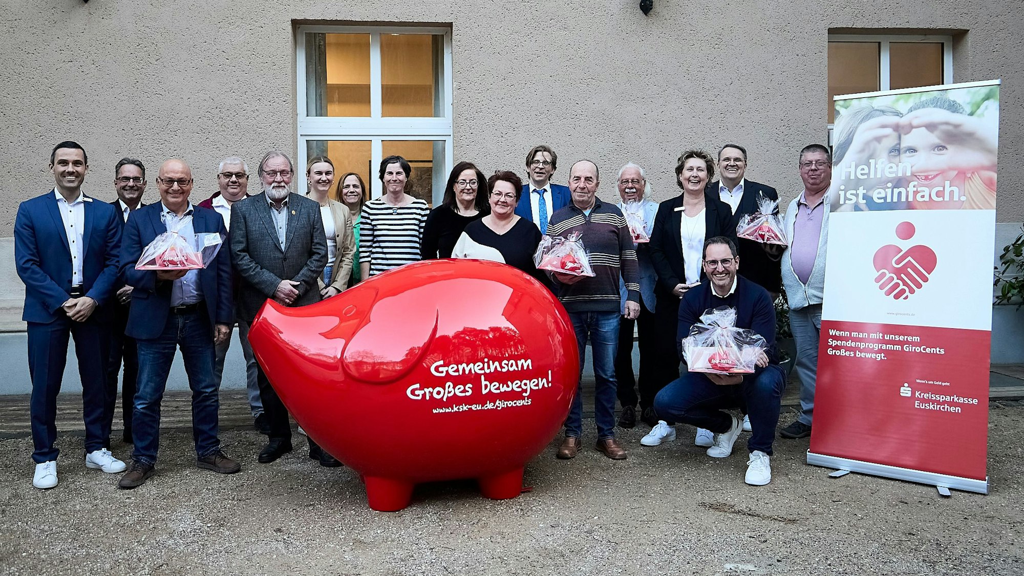 Das Foto zeigt eine Reihe von Frauen und Männern hinter einem überdimensionalen Sparschwein.