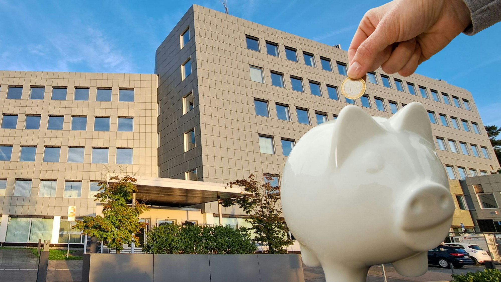 Vor dem Kreishaus des Rheinisch-Bergischen Kreises in Bergisch Gladbach-Heidkamp wirft eine Hand einen Euro in ein Sparschwein.