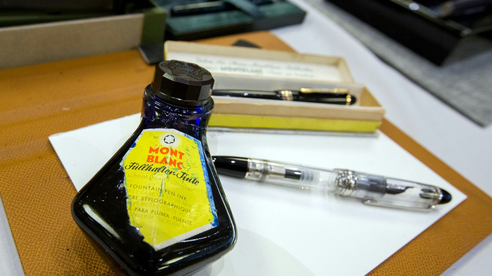 Zwei hochwertige Füllhalter und ein Tintenfass liegen auf einem Bogen Papier.