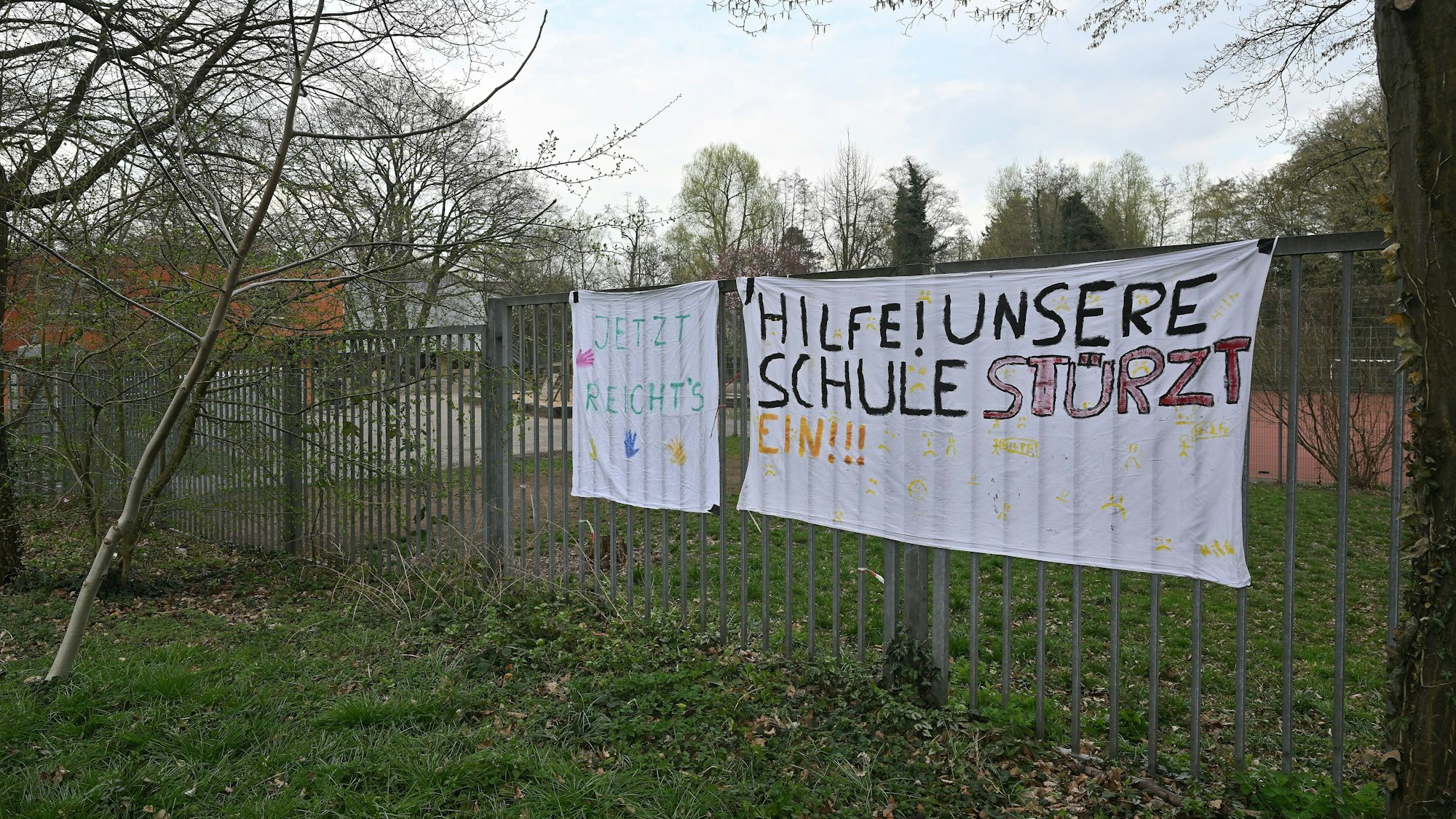 Zwei Plakate hängen an einem Zaun.