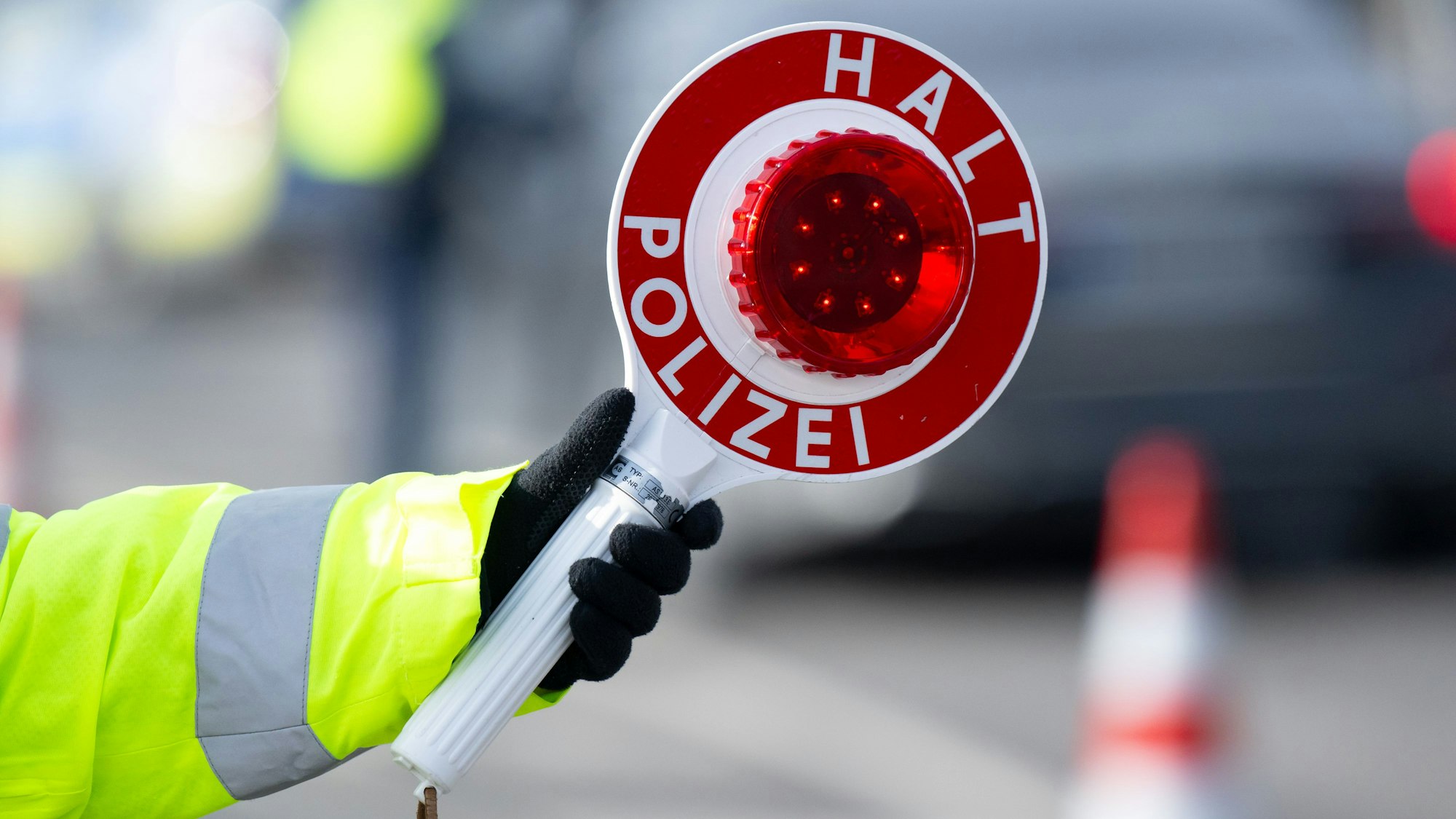 Eine Polizistin kontrolliert an einer mobilen Kontrollstelle und hält dabei eine Polizeikelle mit der Aufschrift „Halt Polizei“ in der Hand.