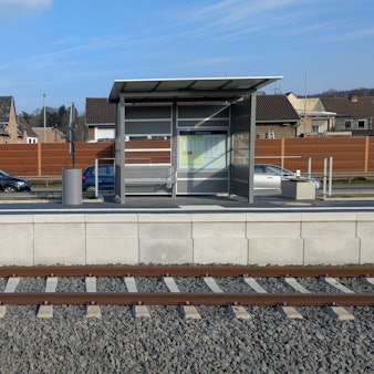 Das Bild zeigt einen Bahnsteig, auf dem sich ein Wartehäuschen, eine Bank und ein Mülleimer befinden.