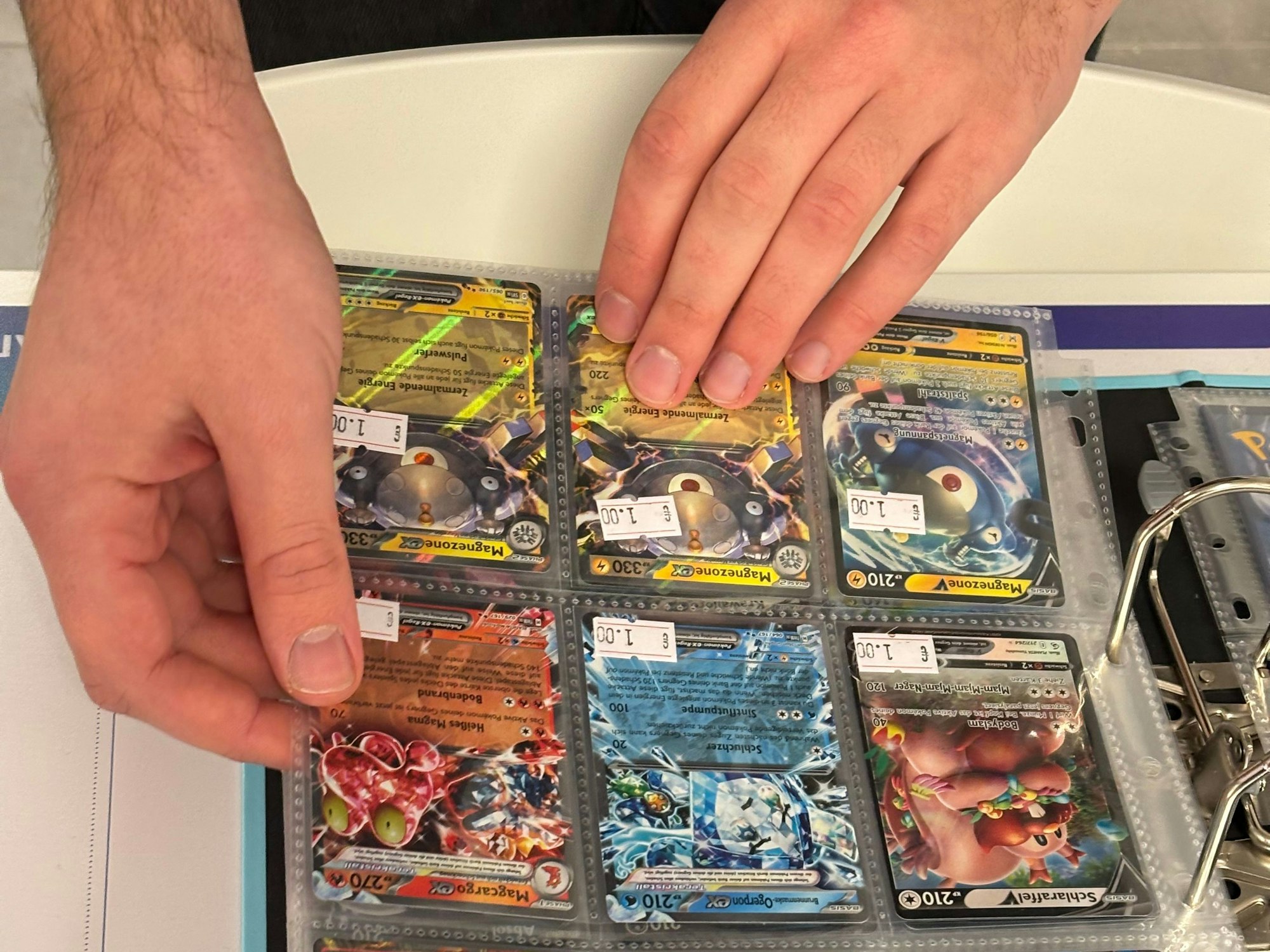 Nahaufnahme auf zwei Hände, die durch einen Ordner mit glitzernden Pokémon-Karten blättern.