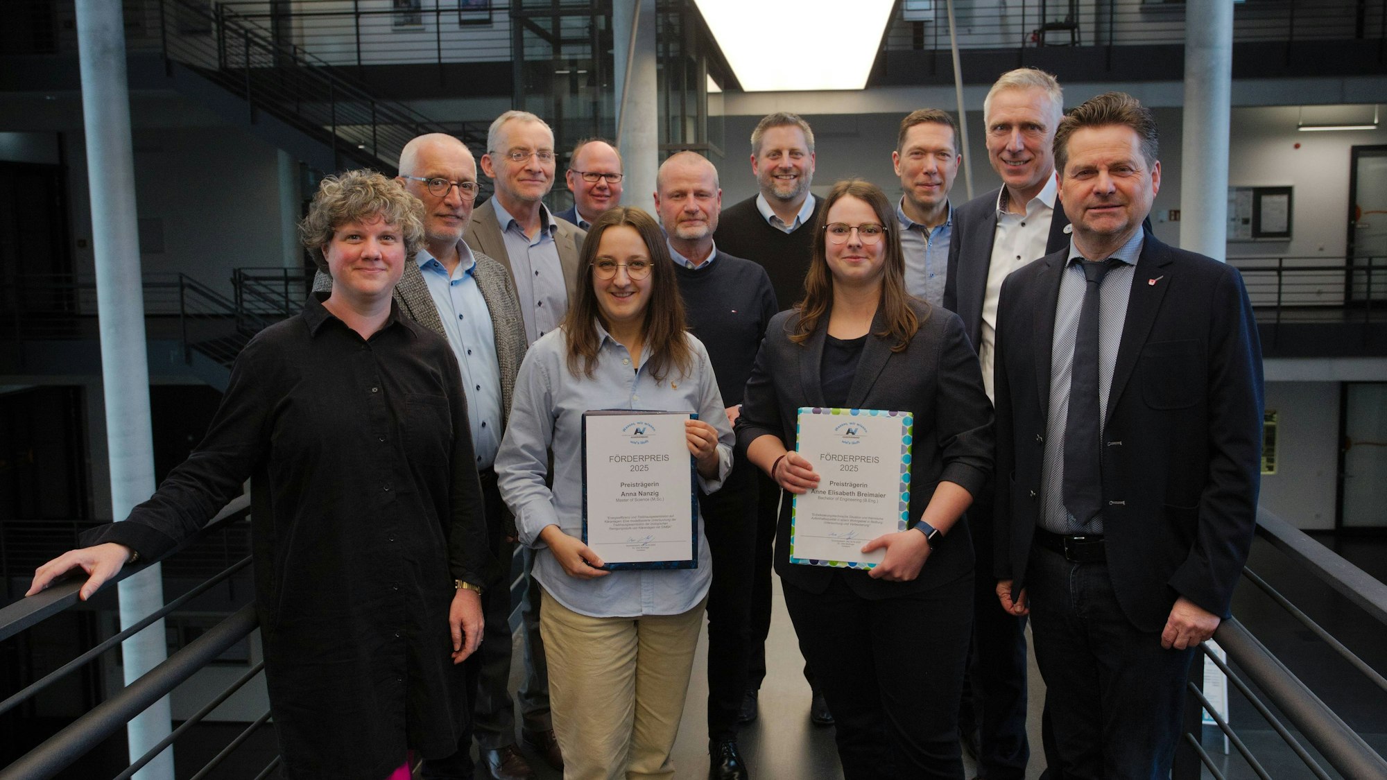 Eine Gruppe von Männern und zwei Studentinnen in der Mitte, die Urkunden in den Händen halten.