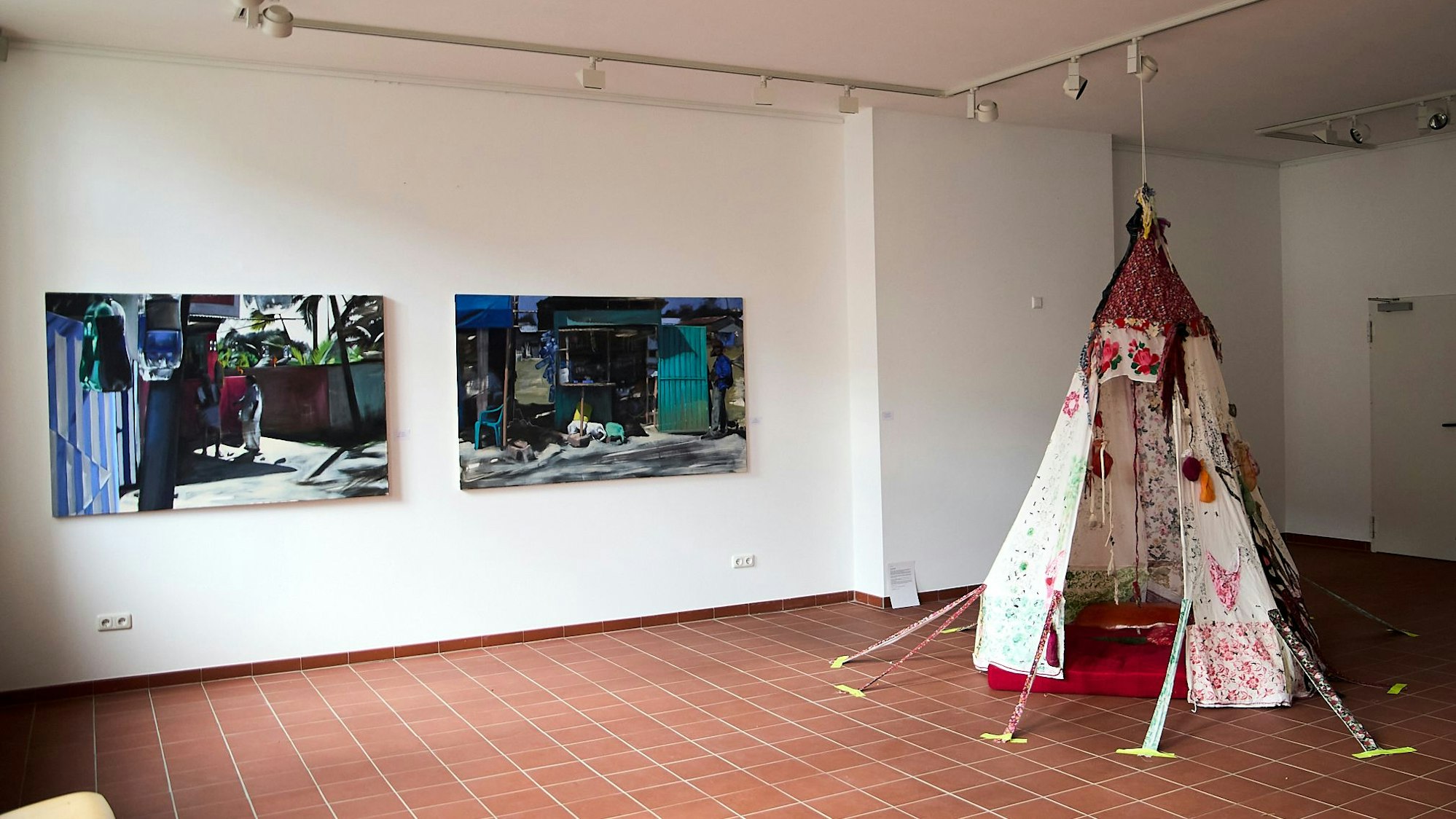 Im Kunstforum Gemünd ist in einer Ausstellung ein buntes Zelt auf dem Boden zu sehen. An den Wänden hängen Bilder.