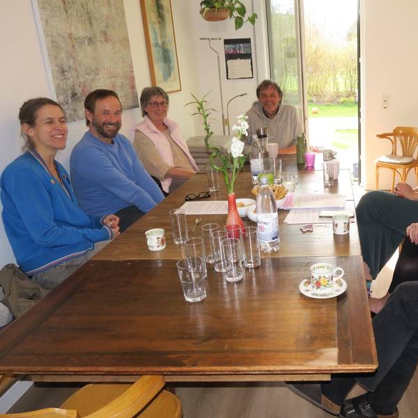 Sieben Personen, von Jung bis Alt, sitzen an einem Küchentisch.