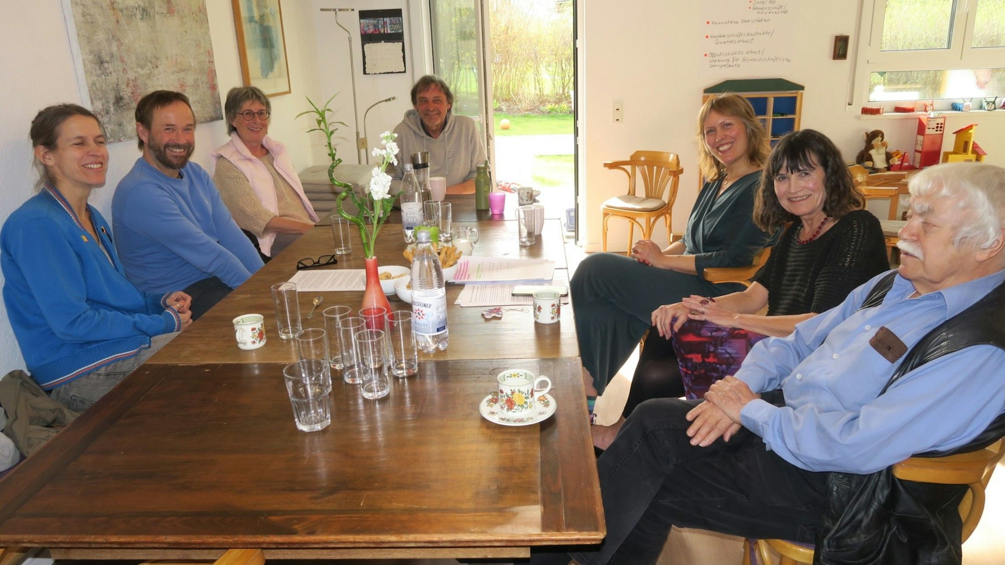Sieben Personen, von Jung bis Alt, sitzen an einem Küchentisch.