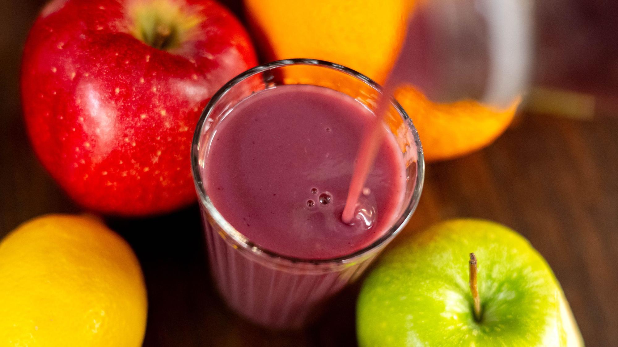 In ein Glas wird ein Smoothie eingegossen. Das Glas steht auf einem Holztisch inmitten von Obst. (Symbolbild)