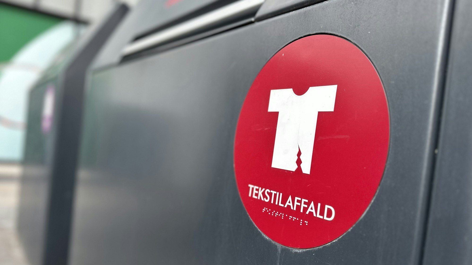 Eine Mülltonne für Textilabfall steht in Kopenhagen vor einem Einkaufszentrum.