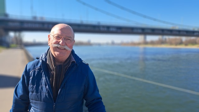 Ein Mann steht vor einer Brücke am Rhein