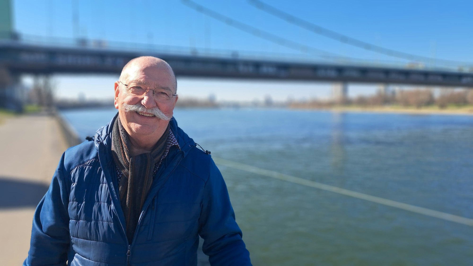 Ein Mann steht vor einer Brücke am Rhein