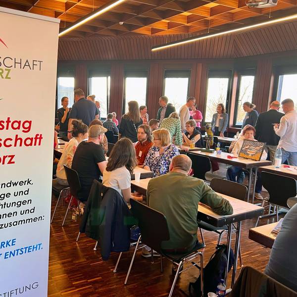 An Konferenztischen sitzen Menschen, andere gehen an den Tischen entlang.