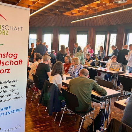 An Konferenztischen sitzen Menschen, andere gehen an den Tischen entlang.